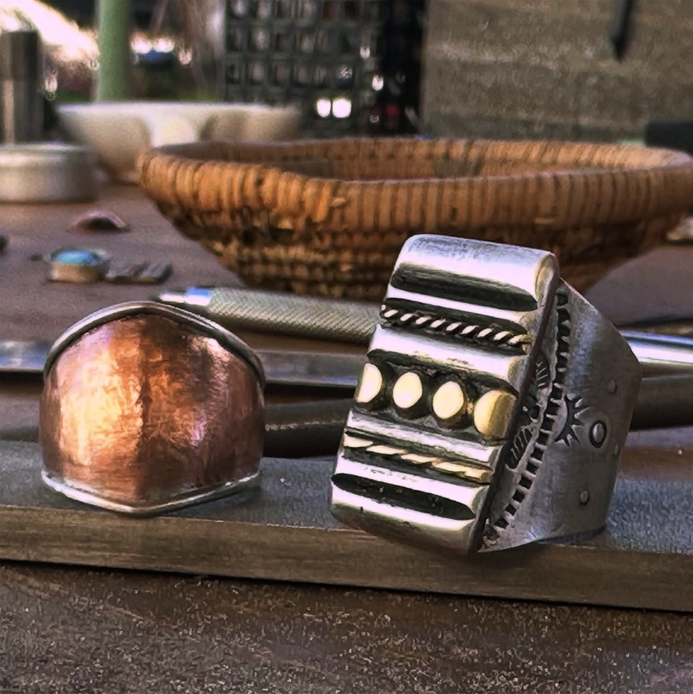Close-up of two mixed metals silver rings with intricate designs on a wooden surface.